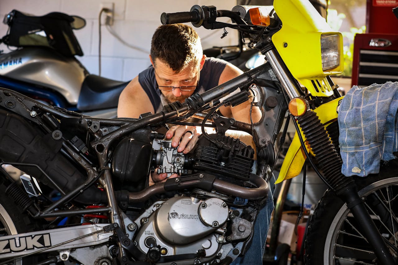A mechanic intensely focused on repairing a motorcycle engine in a cluttered garage setting.