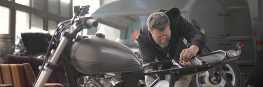 Male mechanic working on a motorcycle in an indoor workshop setting.