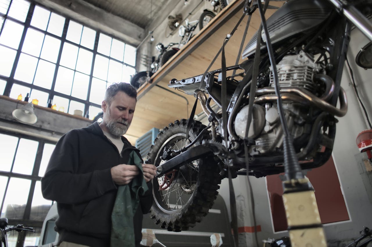 An experienced mechanic working on a motorcycle in a well-lit workshop. Industrial setting with focus on repair and maintenance.