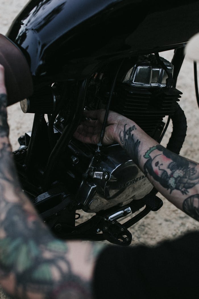 From above of crop faceless male biker with tattooed hands checking motor of motorcycle before riding