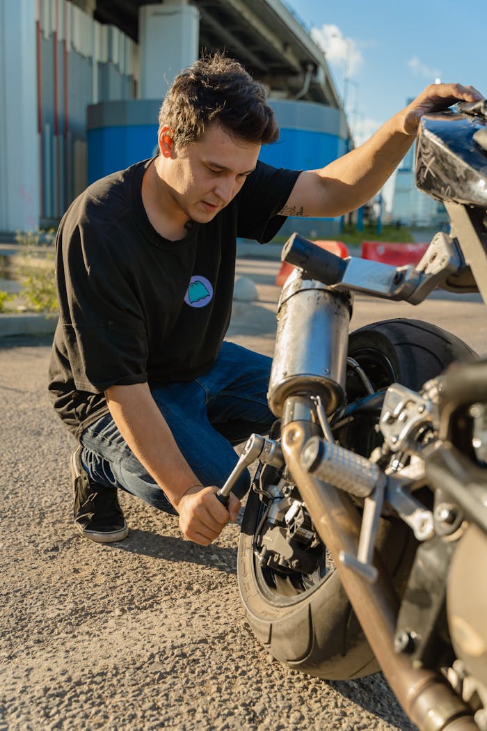 A young man working on a motorcycle outdoors, showcasing maintenance skills under a clear sky.