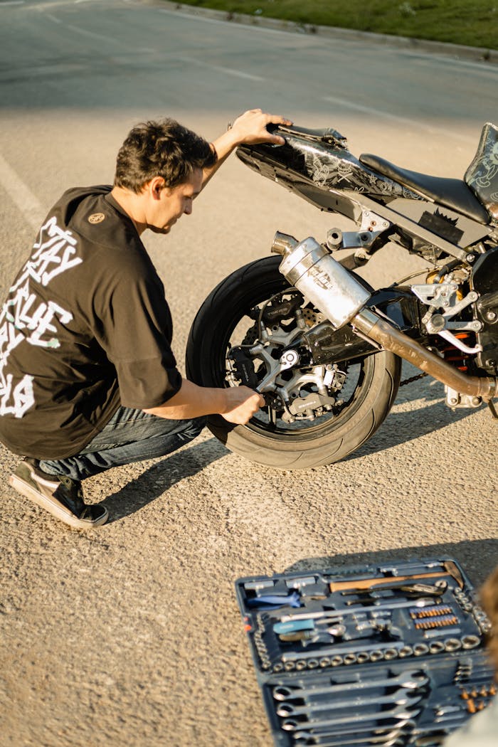 A man fixing a motorcycle with a tool kit on the roadside during the day.