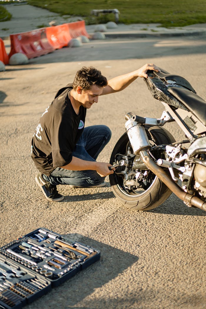A man working on motorcycle repairs with tools on a bright outdoor day.
